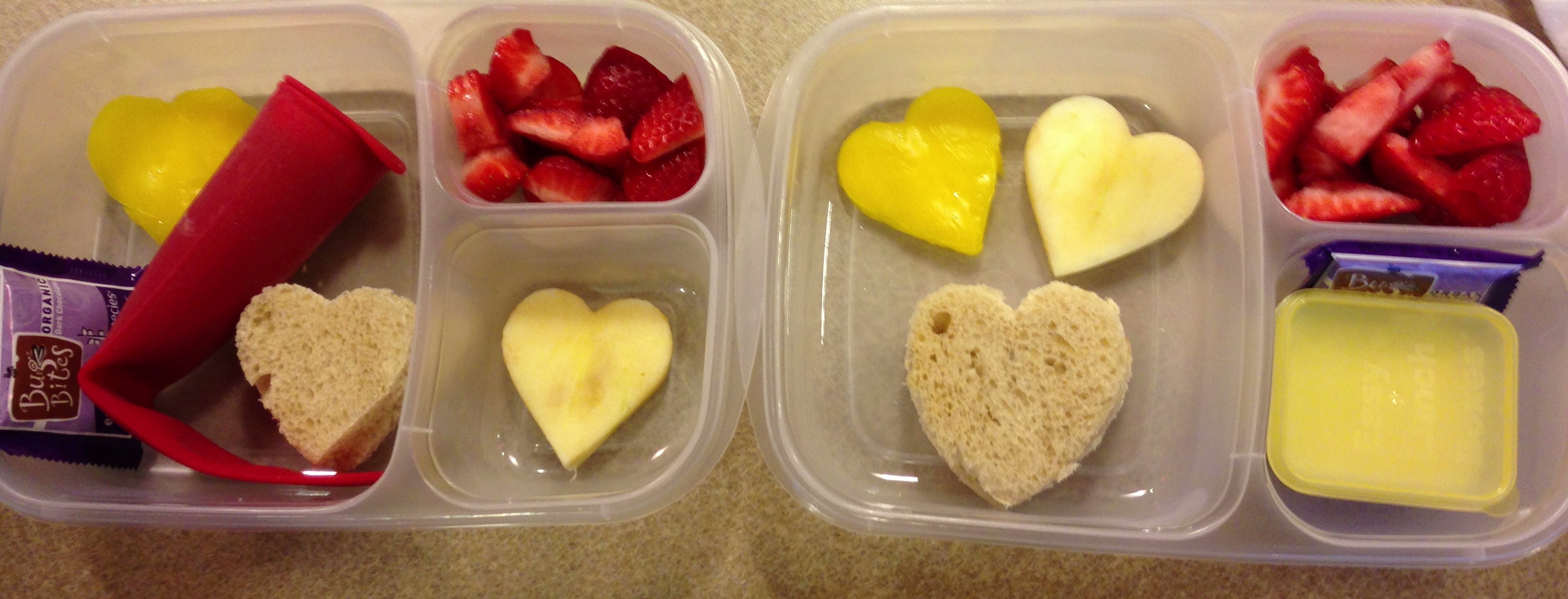 Heart shaped pb & j, heart shaped apple slices, and a heart shaped yellow pepper slice, strawberries. Yogurt smoothie in red squeeze tube and a piece of dark chocolate as a special treat! All ingredients organic.
